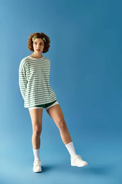 A young woman with short curly hair poses confidently in a vibrant outfit against a blue background. — Stock Photo