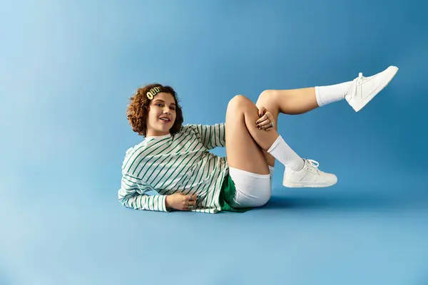 Una joven con el pelo rizado posa juguetonamente en su traje vibrante sobre un telón de fondo azul. — Stock Photo