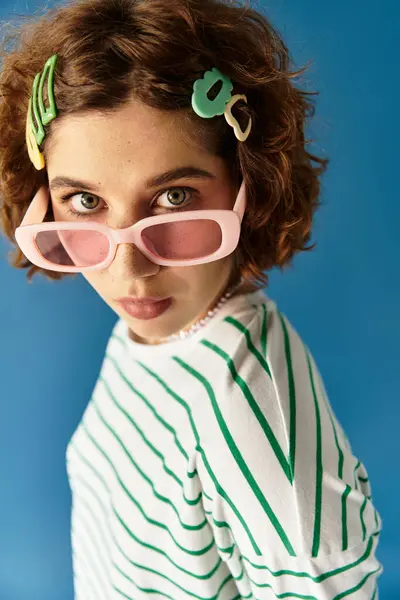 A young woman with curly hair shows off her vibrant outfit and playful clips against blue. — Stock Photo