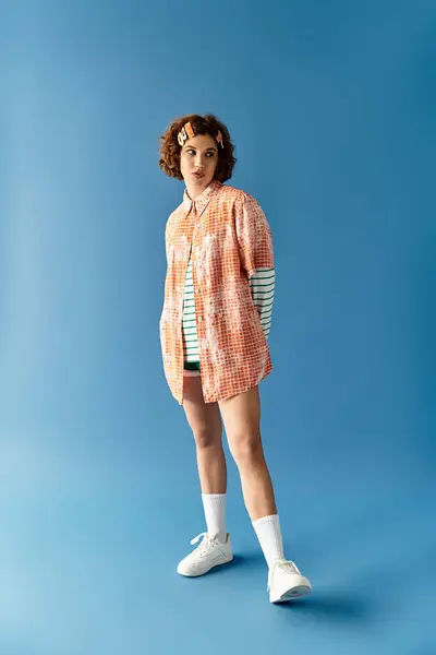 A young woman with short curly hair showcases her vibrant summer outfit on a bright blue background. — Stock Photo