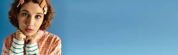 A young woman with short curly hair poses thoughtfully in a bright outfit against a blue background, banner — Stock Photo