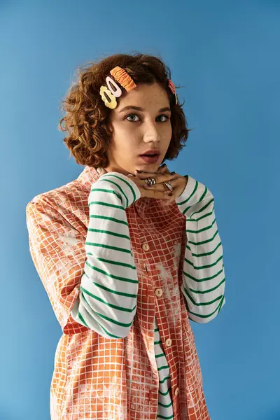 A young woman with curly hair showcases her vibrant outfit, striking a playful pose against blue. — Stock Photo