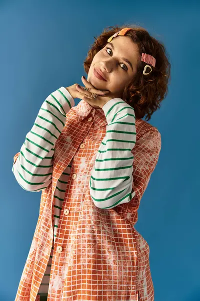 A young woman with curly hair exudes joy in a playful outfit while posing against a blue background. — Stock Photo