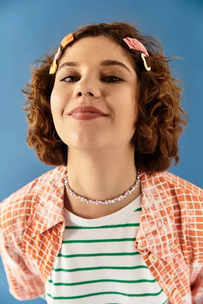 A young woman with short curly hair showcases her vibrant summer outfit against a blue background. — Stock Photo