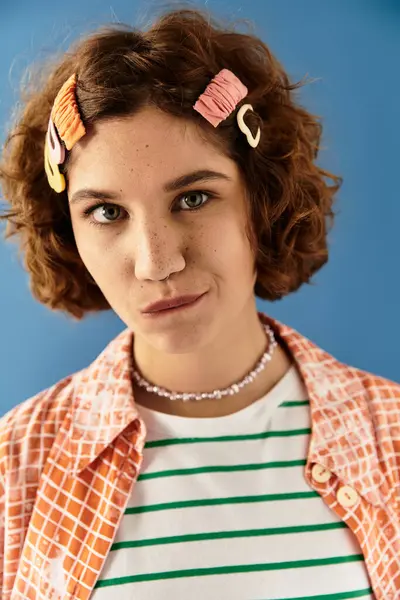 A young woman confidently poses in a colorful outfit with cute hair clips against a blue backdrop. — Stock Photo