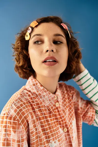 A young woman with short curly hair showcases her vibrant outfit against a blue background. — Stock Photo