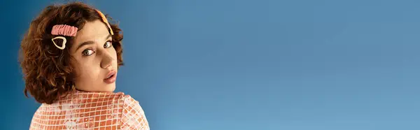 A young woman with short curls poses playfully in a vibrant outfit against a blue backdrop, banner — Stock Photo