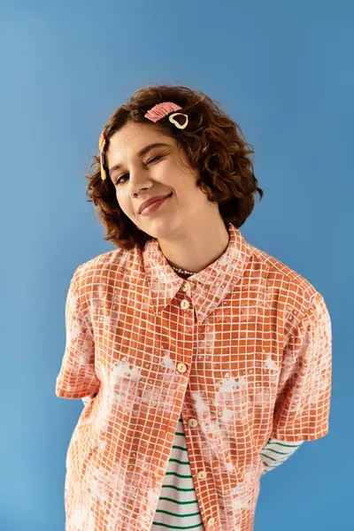 A young woman with short curly hair playfully poses in a colorful outfit on a blue backdrop. — Stock Photo