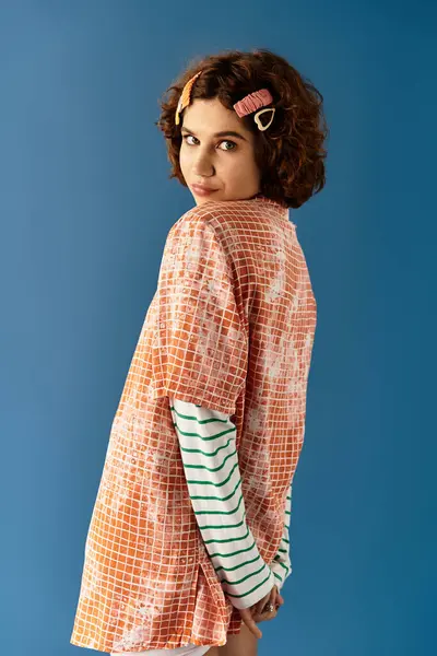 A young woman with curly hair confidently poses in a vibrant outfit against a blue backdrop. — Stock Photo