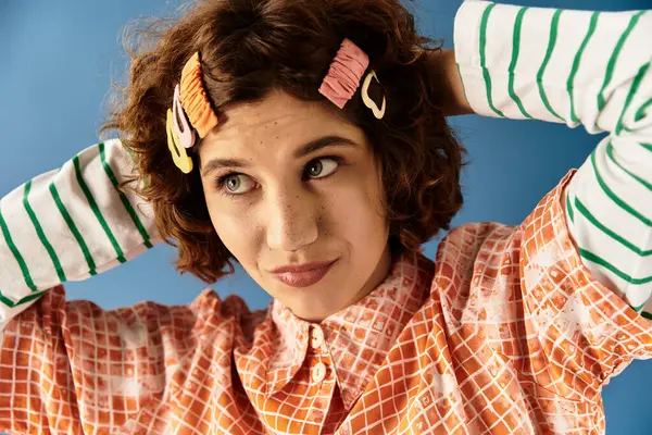 Une jeune femme met en valeur son style aux cheveux bouclés et une tenue colorée sur fond bleu. — Photo de stock