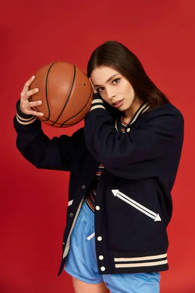 Confident woman poses with a basketball, embodying fashion and athleticism against a bold backdrop. — Stock Photo