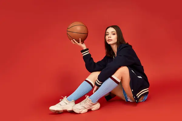 A young woman in trendy sportswear poses confidently while balancing a basketball. — Stock Photo