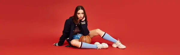 Mujer joven muestra su aspecto elegante, sentada casualmente con una pelota de baloncesto e irradiando confianza. — Stock Photo