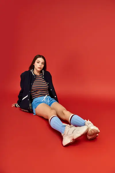 A stylish woman lounges comfortably against a bright red background, showcasing her trendy outfit. — Stock Photo