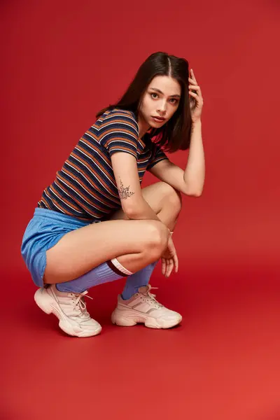 Stylish woman poses playfully in vibrant attire, highlighting her unique fashion sense against red. — Stock Photo