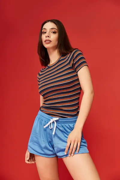 Une jeune femme modèle des vêtements colorés avec un équilibre confiant sur un fond rouge frappant. — Photo de stock