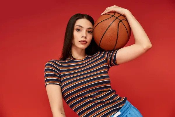 A beautiful woman poses confidently against a striking red background while holding a basketball. — Stock Photo