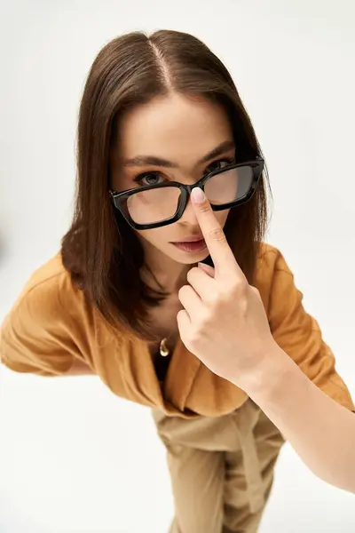 Confident woman in chic attire playfully adjusts her glasses while striking a pose indoors. — Stock Photo