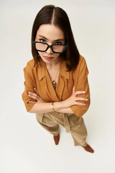 Young woman in chic attire with glasses poses confidently in a minimalist studio environment. — Stock Photo