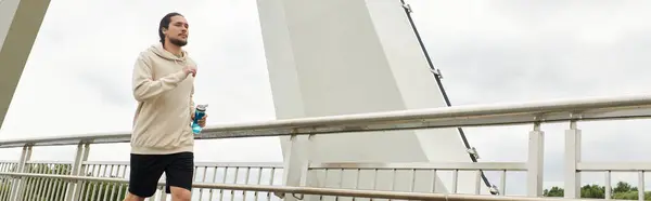 Молодой спортсмен в толстовке бегает по мосту, обнимает фитнес и свежий воздух, баннер — стоковое фото