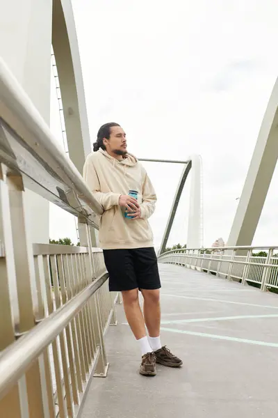 A young athletic man in a hoodie takes a break on a bridge while exercising outdoors. — Stock Photo