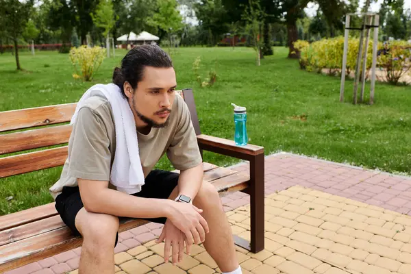 Un joven con barba se sienta en un banco, reflexionando después de una intensa rutina de ejercicios al aire libre. - foto de stock