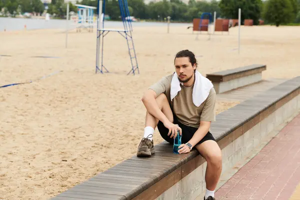 Fit young man with a beard rests on a wooden bench after an outdoor workout at the beach. — Stock Photo