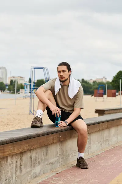 Young man enjoys a moment of rest while exercising at a beachside park during cloudy weather. — Stock Photo