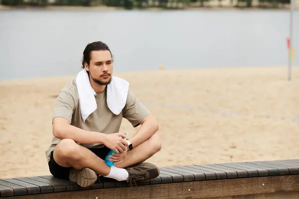 Giovane uomo gode di una pausa durante l'esercizio in spiaggia, riflettendo sul suo viaggio di fitness. — Foto stock