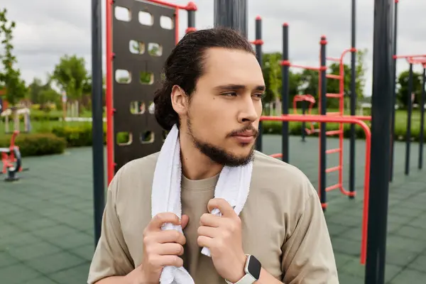 Un joven se para al aire libre con una toalla alrededor de su cuello, enfocada en su rutina de entrenamiento. - foto de stock