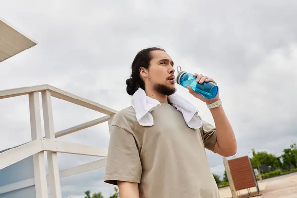 Young man with a beard enjoys a hydration moment after exercising outdoors in nature. — Stock Photo