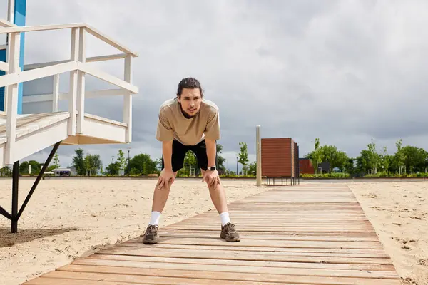 A young sporty man pauses to catch his breath while exercising outdoors near the beach. — Stock Photo