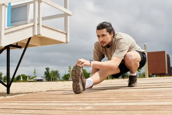 A bearded young man stretches on a wooden deck, getting ready for his workout. — Stock Photo