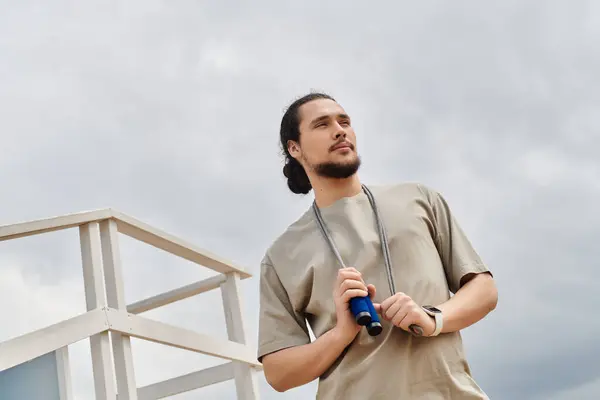 Young man with a beard stands outdoors, holding workout gear, focused on fitness and wellness. — Stock Photo