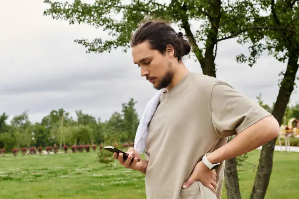 A fit young man with a beard is working out in an outdoor park, focused on his phone. — Stock Photo