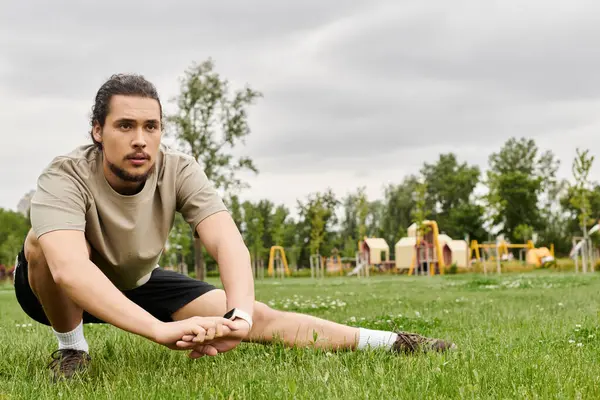 A fit young man with a beard stretches on the grass in a park, ready for his workout. — Stock Photo