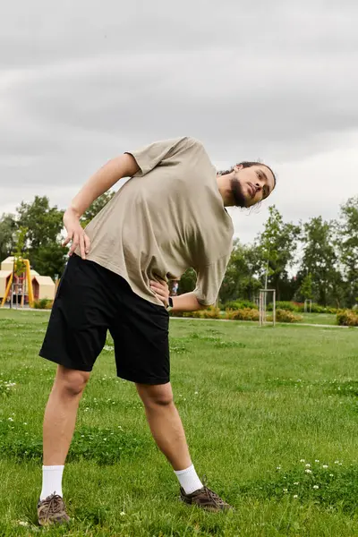Young athletic man performs stretching exercises in a grassy area under a cloudy sky. — Stock Photo
