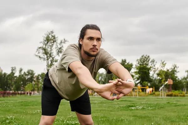 A young man with a beard engages in stretching exercises while surrounded by nature. — Stock Photo
