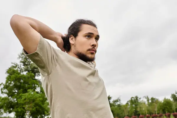 A fit young man with a beard stretches his arms in a natural environment, preparing for exercise. — Stock Photo