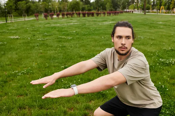 A young man exercises outside, performing squats while enjoying the fresh air and greenery. — Stock Photo