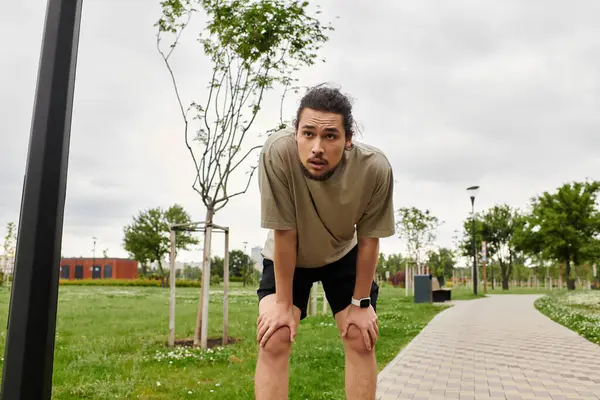 A young man catches his breath while exercising in the park, showing his fitness dedication. — Stock Photo
