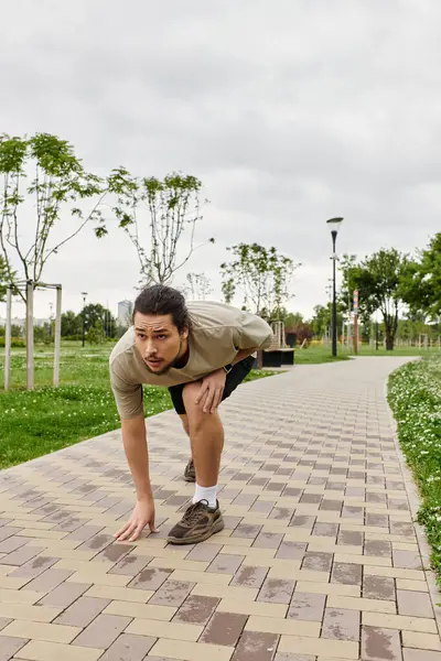 A young man with a beard crouches in a park, ready to begin an outdoor workout while staying fit. — Stock Photo