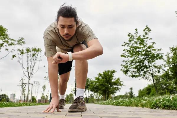 Young man with a beard checks his fitness tracker while preparing to exercise outdoors. — Stock Photo