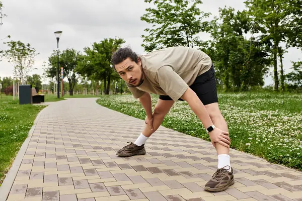 Sporty individual prepares for exercise by stretching in a lush park on a cloudy day. — Stock Photo