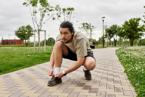 A young man prepares for his workout outdoors by tying his shoelaces in a park. — Stock Photo