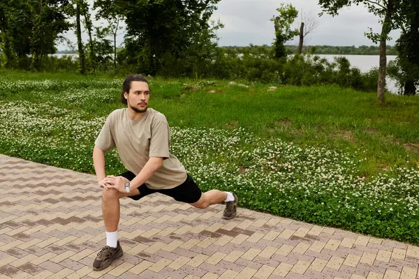 A fit young man stretches outdoors by a tranquil water surrounded by greenery. — Stock Photo