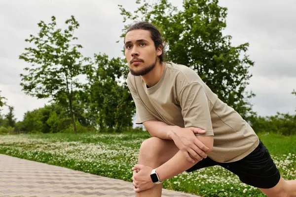 A fit young man with a beard is stretching outdoors, preparing for an exercise session in nature. — Stock Photo