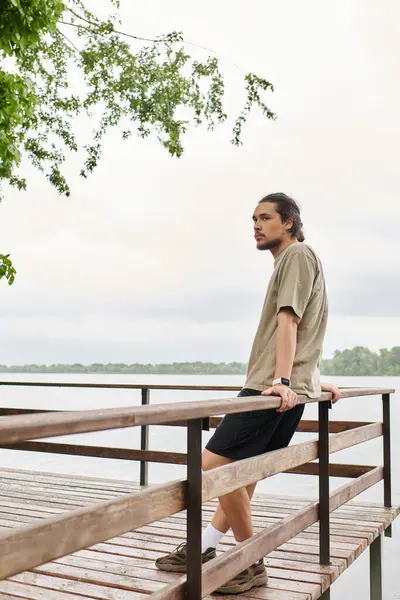 A sporty young man with a beard leans on the railing, enjoying an outdoor workout by the water. — Stock Photo