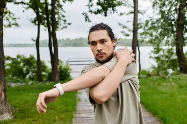 A young man focuses on stretching his arms while enjoying a refreshing workout outside by the water. — Stock Photo