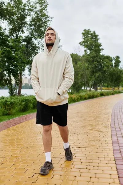 A young man in a hoodie walking along a scenic path by the water. — Stock Photo